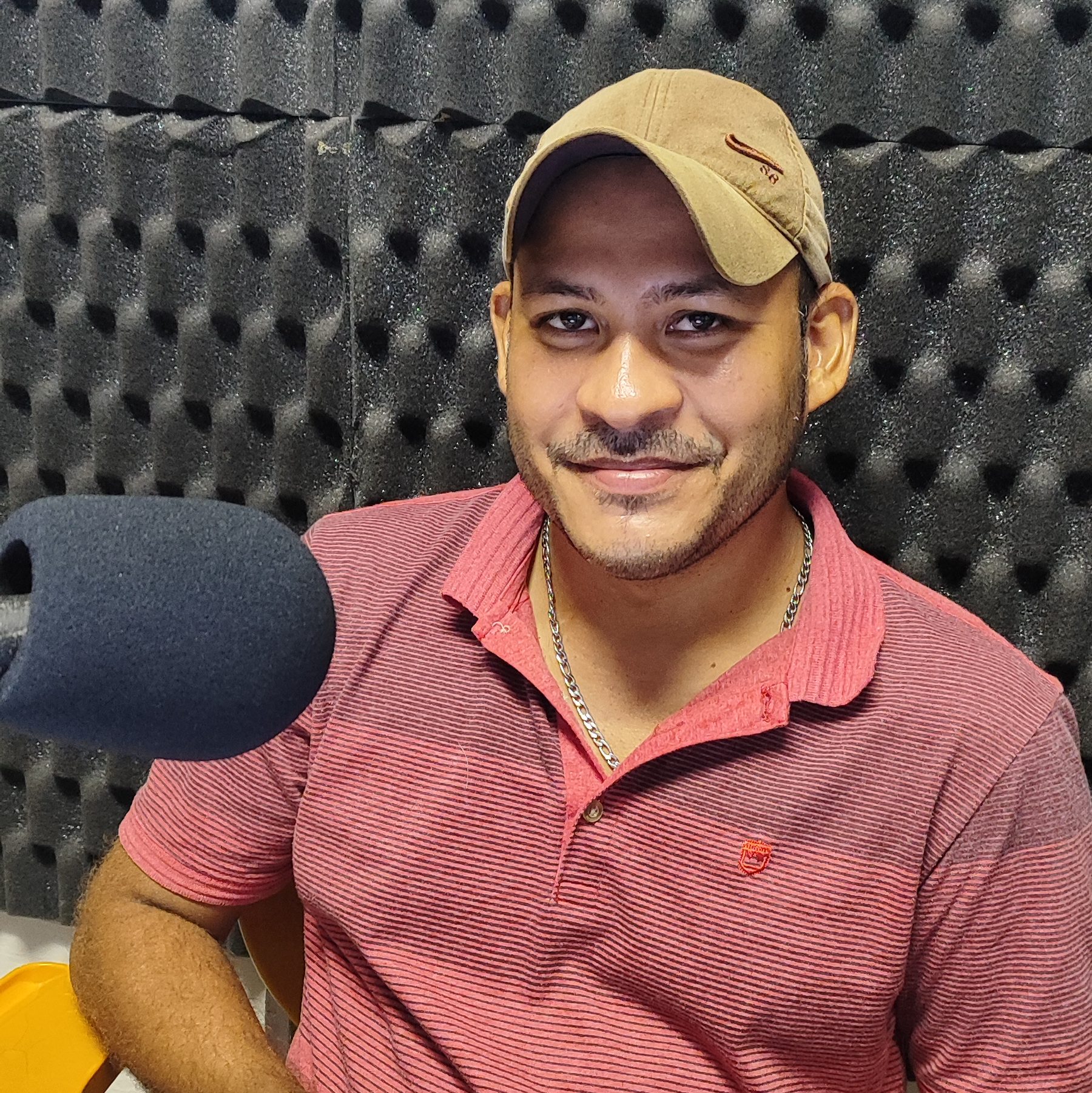 Foto de Kelton Golden. Jovem negro não retinto. Ele usa um boné marron e veste camisa vermelha. À sua direita um microfone.